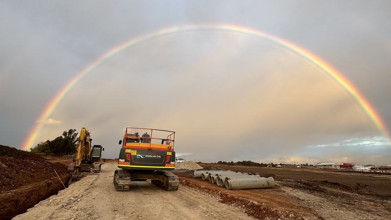 Rainbow over a Douglass Civil excavator on site, with concrete stormwater pipes stacked ready to go in