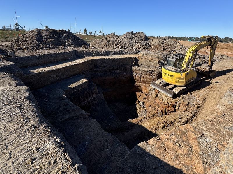 Deep benched excavation with stepped walls, a Sumitomo excavator working on the edge