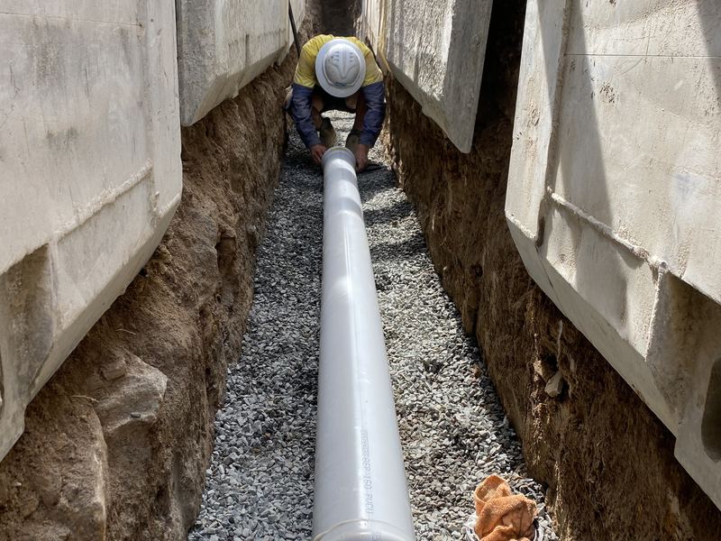 Pipe being laid on gravel bedding inside a shored trench with a steel shoring box, Western Sydney