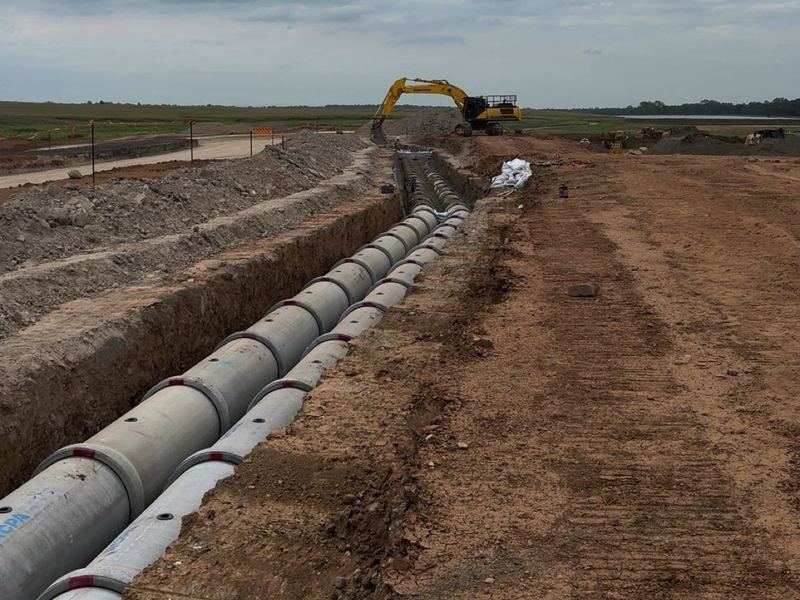 Twin concrete stormwater pipe runs laid side by side in a long trench, excavator at the far end